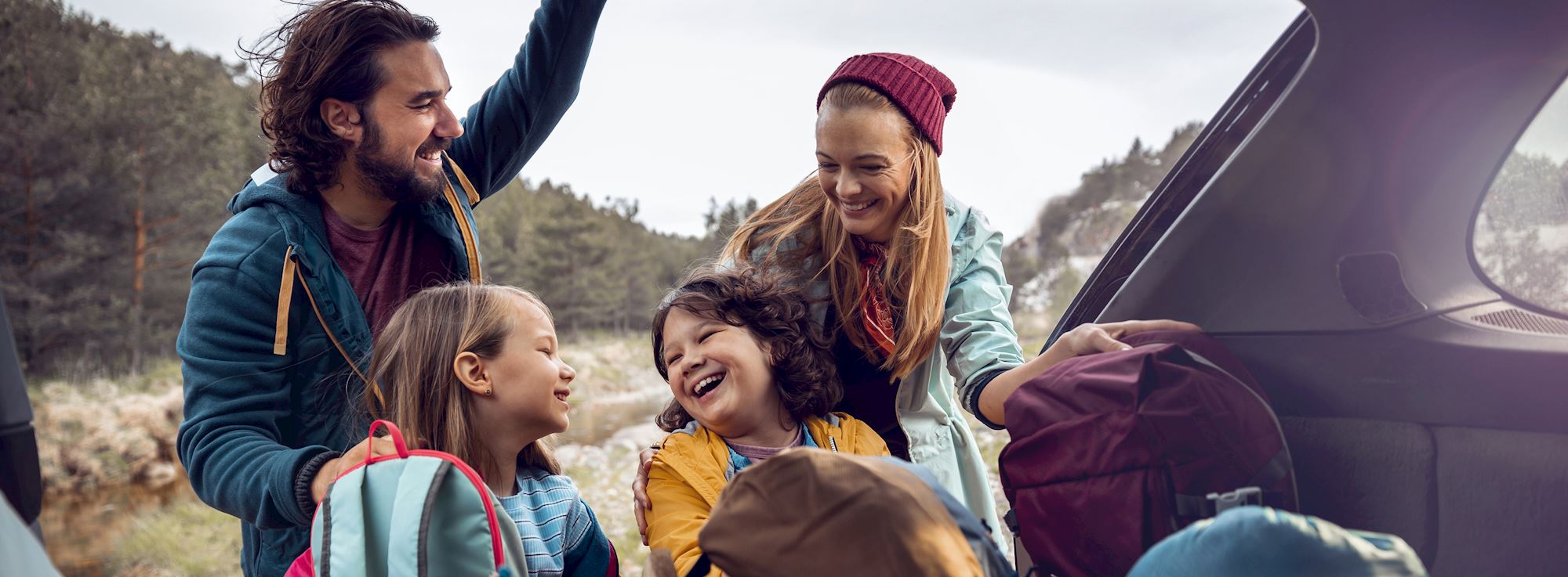 Happy and smiling young family getting camping gear out of the car